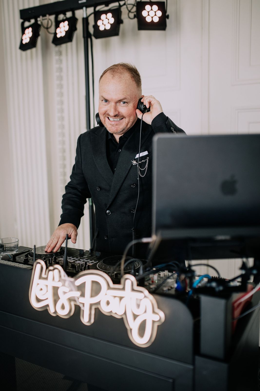 Hochzeits-DJ Andy lachend am DJ-Pult mit Let's-Party-Neonschild